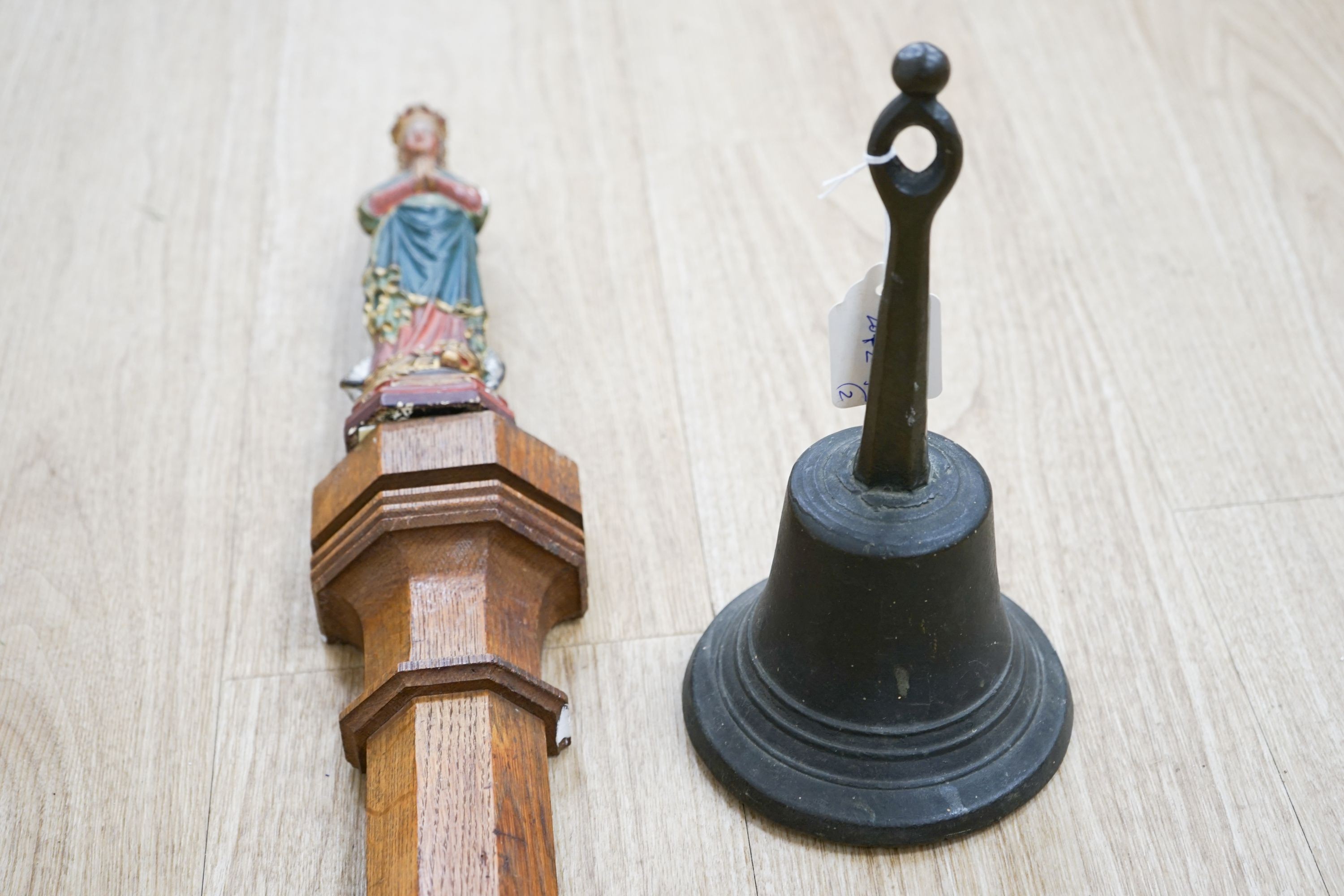 An early hand bell and a religious figure on an oak pilaster 65cm